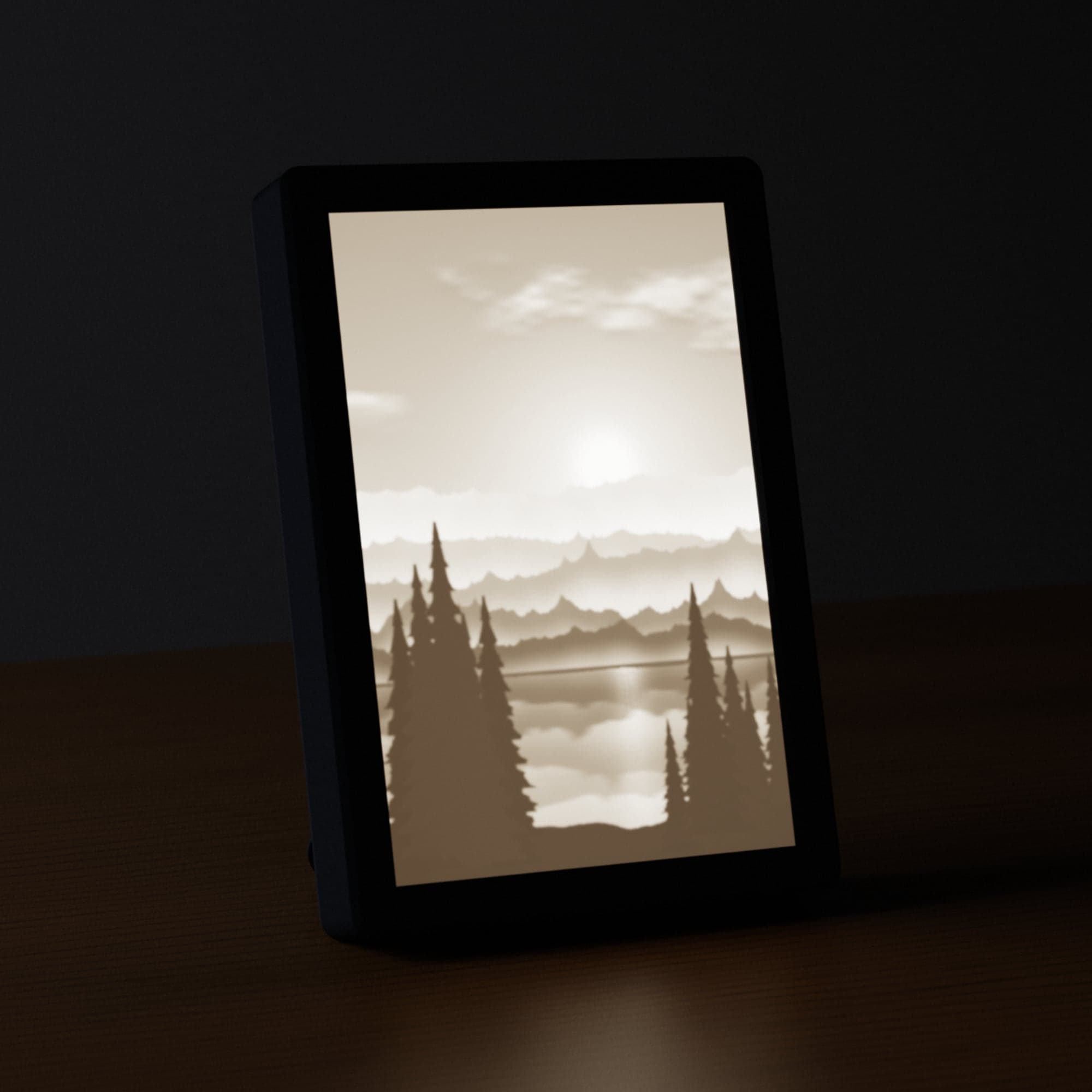 A Monochrome Lithophane of a mountain lake at sunrise, lit from behind in a black frame on a desk
