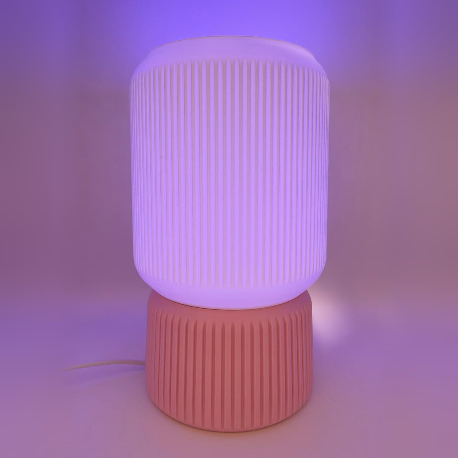 A LEAH lamp lit purple: a white ribbed shade on a pink ribbed base